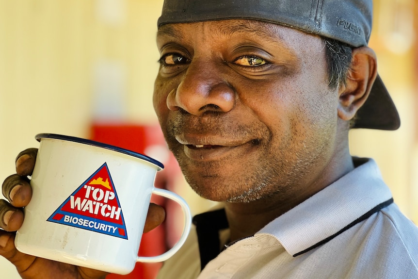 A smiling man holds up a mug saying 'Top Watch Biosecurity'