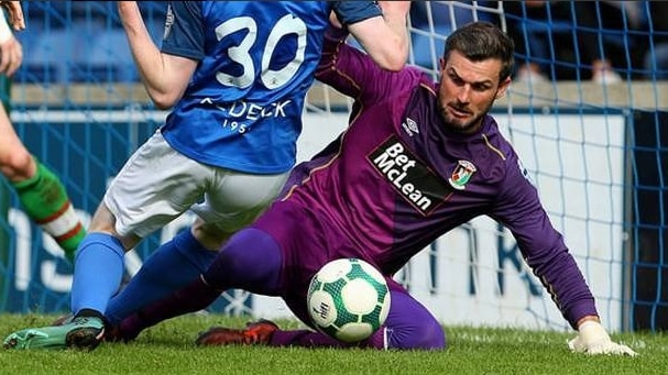 A man wearing purple dives towards the ball with a man in blue running towards him