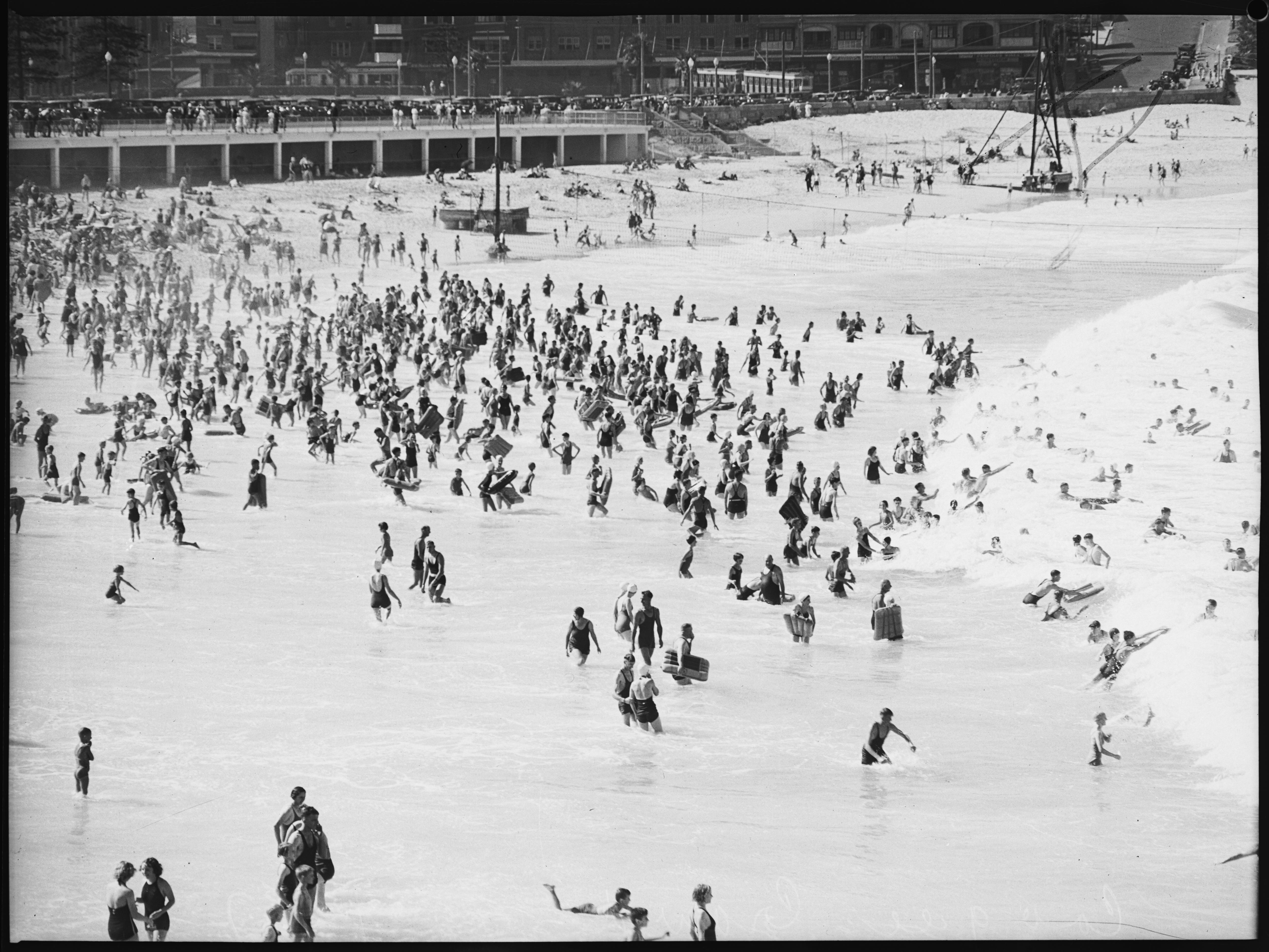 a black and white photo of beachgoers with two concrete structure towards the back