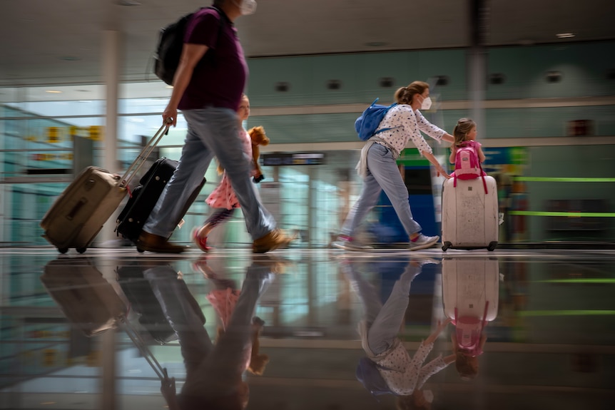 People carrying bags and pulling along suitcases while walking at an airport.