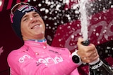 A man in cycling gear sprays champagne from a stage.