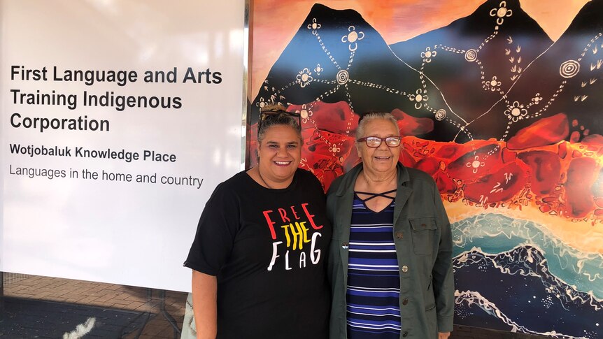 Two women stand in front of a glass shopfront that has 'First Languages and Arts Training Indigenous Corporation' written on it 