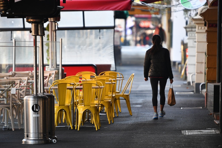 Person walks past yellow chairs on footpath 