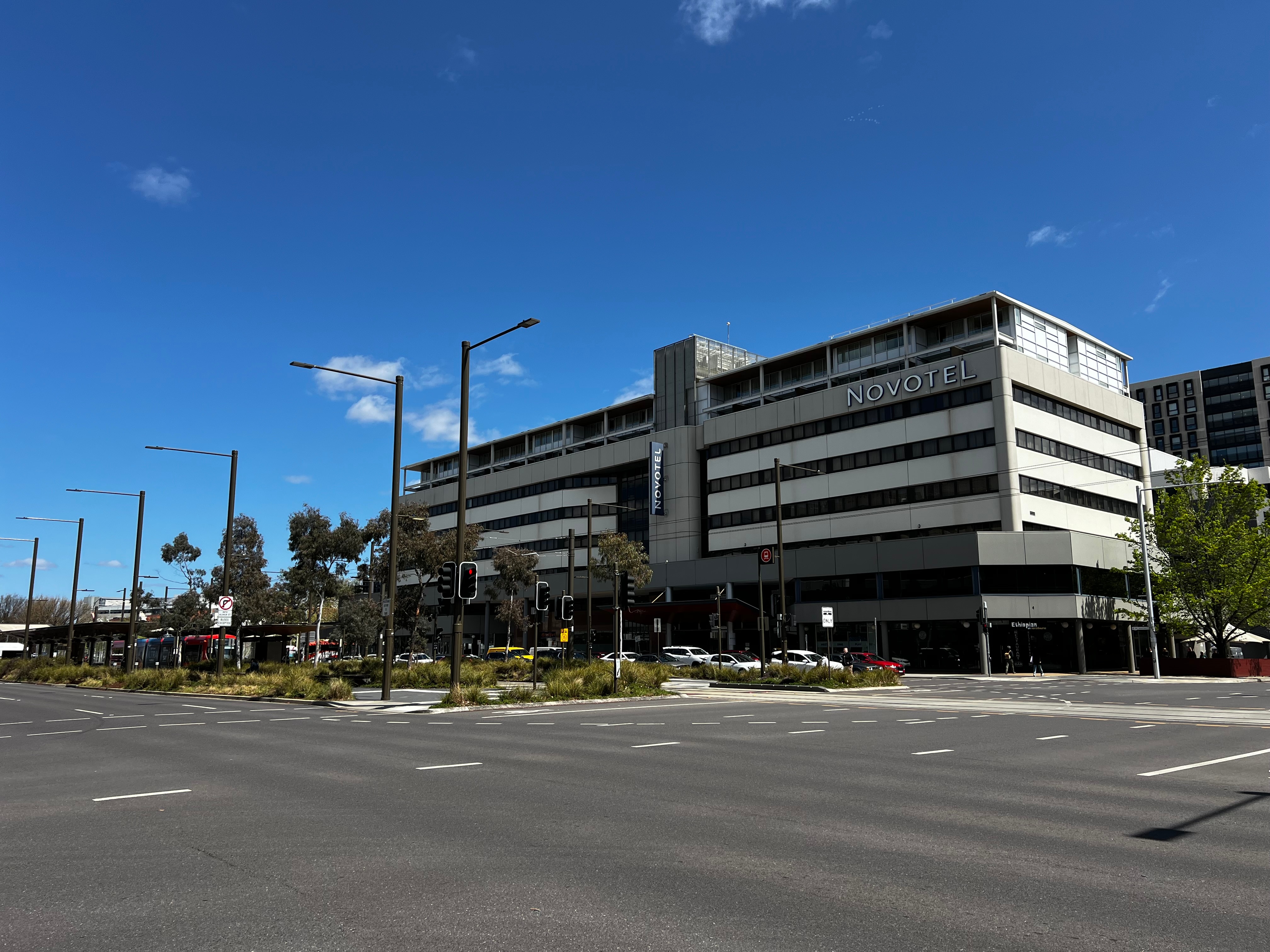 The exterior of a multi-storey building that reads "Novotel" behind a six-lane traffic light intersection.