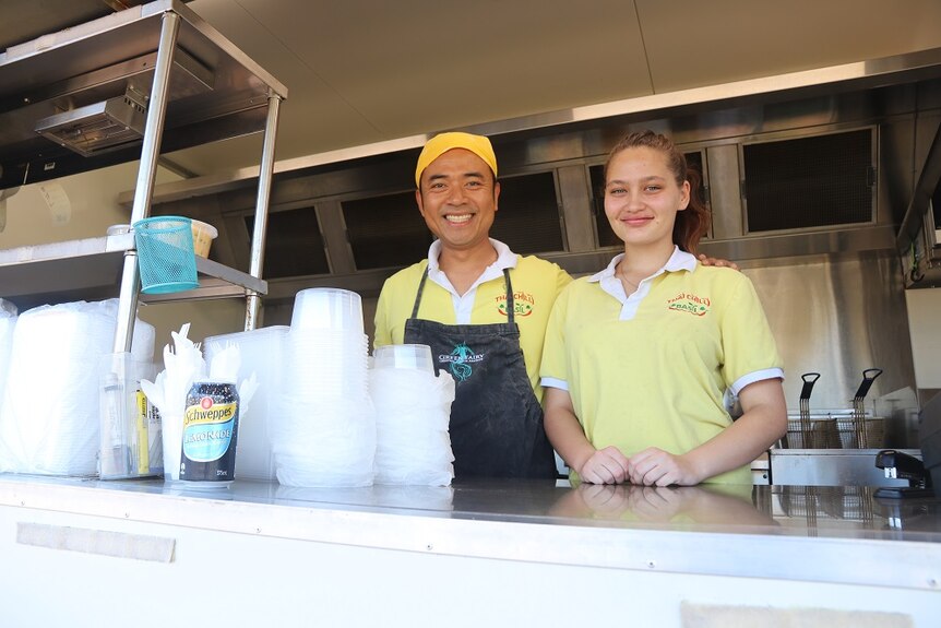 Two people stand inside a food truck and smile