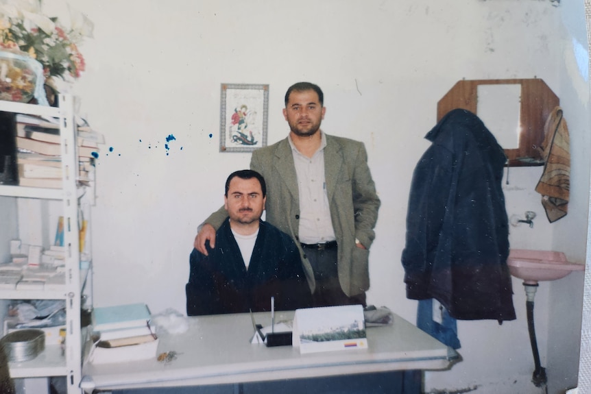 An old colour photo of two men at a doctor's clinic looking at the camera unsmiling 