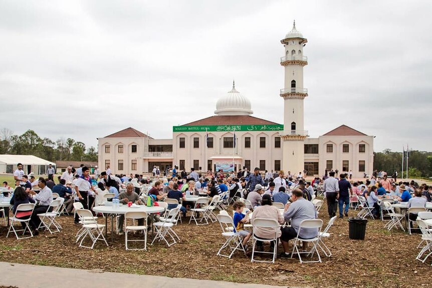 The view of the Ahmadiyya mosque from the outside. It's white, with a dome and minaret. People are pictured sitting outside.