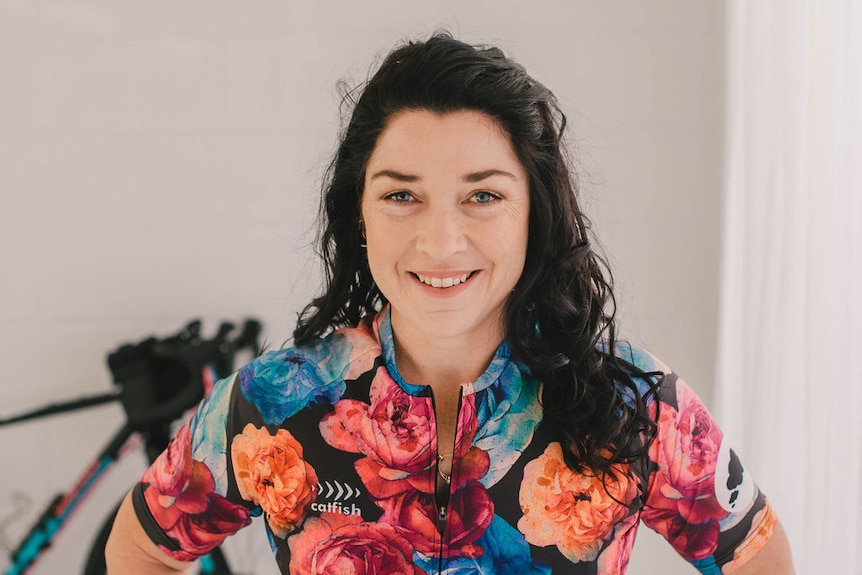 mid shot of female cyclist in floral race wear in foreground, blurred bike in background