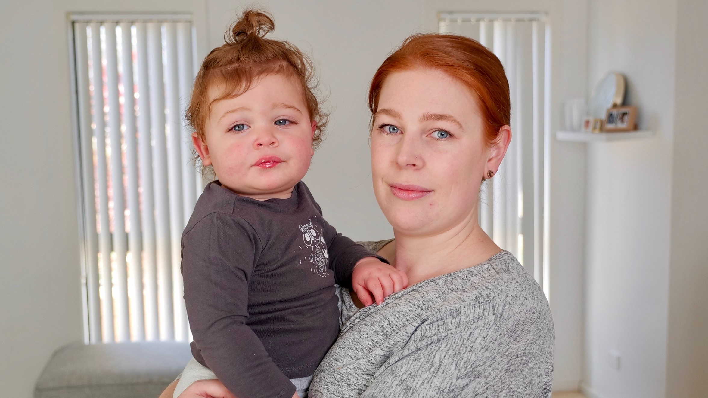 Sarah looks into the camera, holding her toddler.