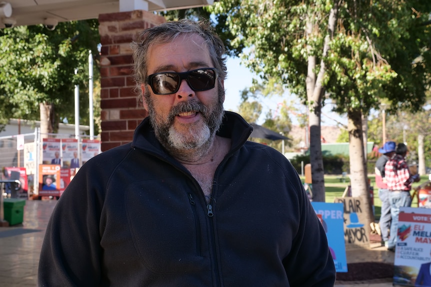 A man in sunglasses standing outside a building under trees