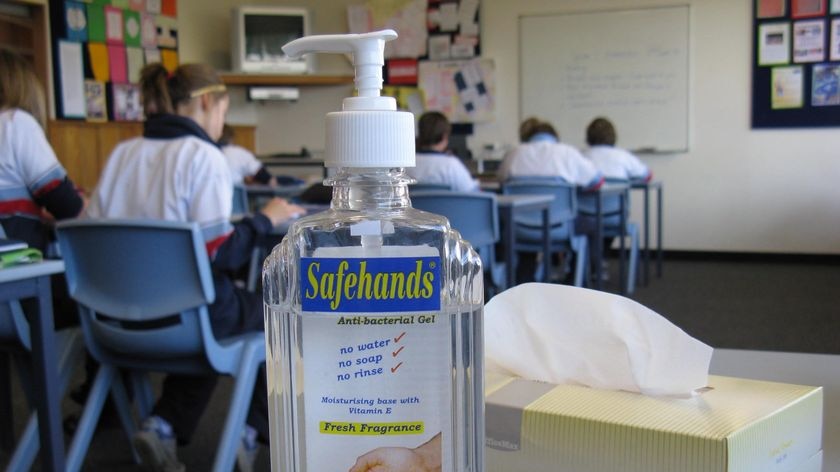Swine flu anti-bacterial gel and tissues on a desk with unidentified students behind.
