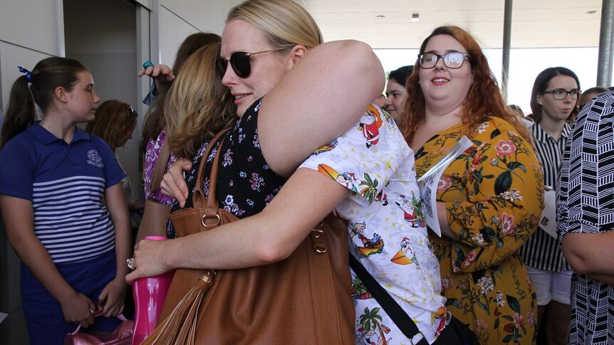 Two woman stand in a crowd and hug.
