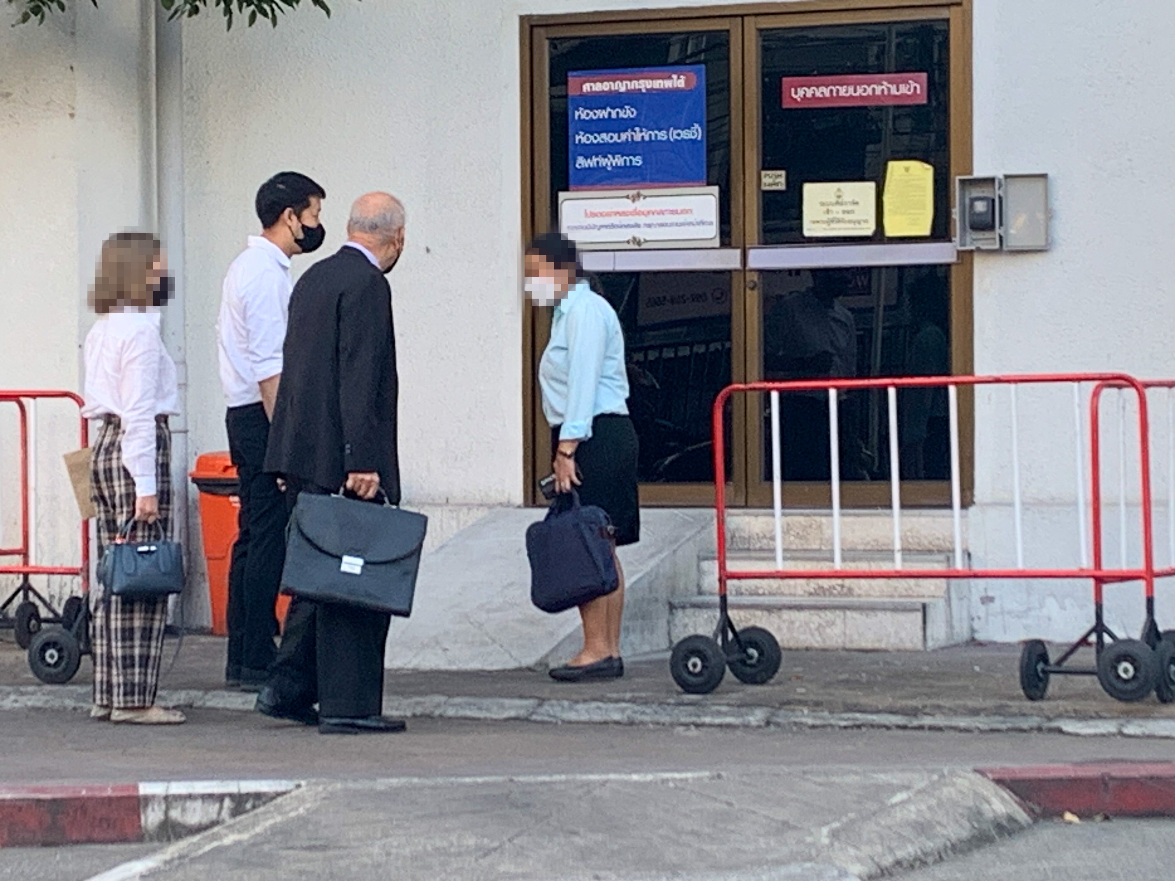 Four people outside a sliding door, one older man in a suit carrying a briefcase, a younger man next to him, and two women
