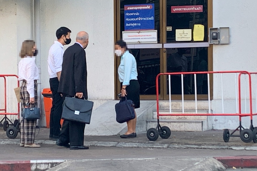 Four people outside a sliding door, one older man in a suit carrying a briefcase, a younger man next to him, and two women
