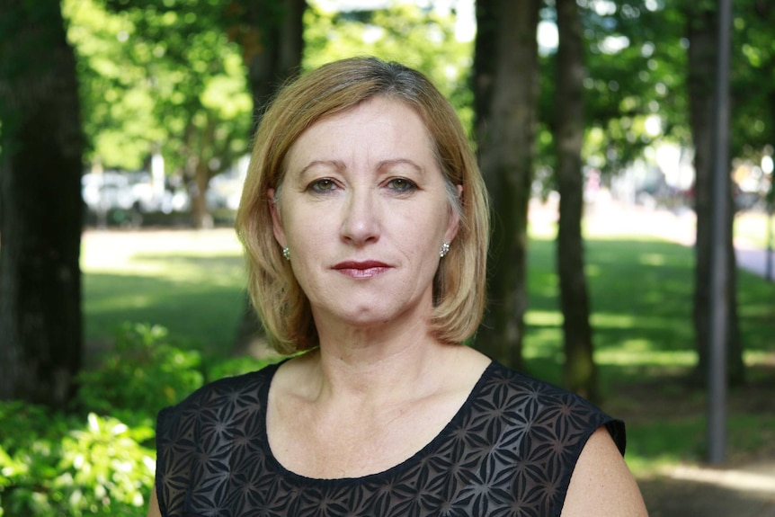 A woman with a blonde bob haircut looks straight at the camera.