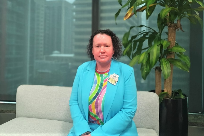 A woman wearing a bright blue blazer, sitting on a couch