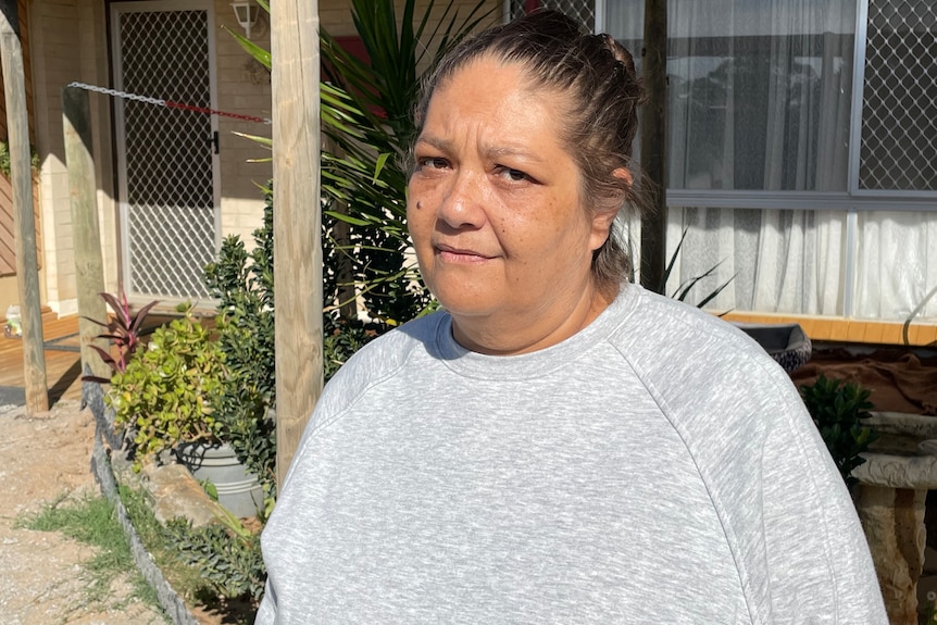 Woman with her hair pulled back, wearing grey windcheater smiles at the camera in front of a house