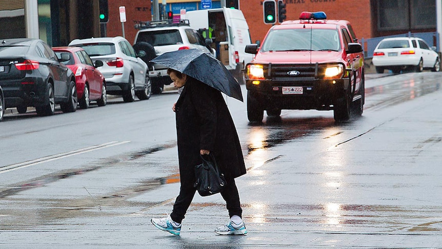 An elderly woman crosses a wet road in Burnie, Tasmania.