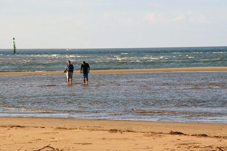 Two men walk in a shallow section of the ocean