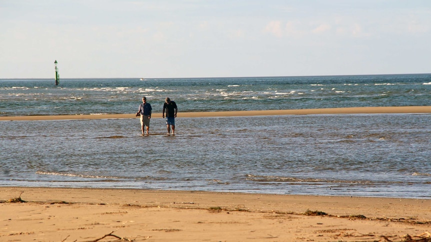 Two men walk in a shallow section of the ocean