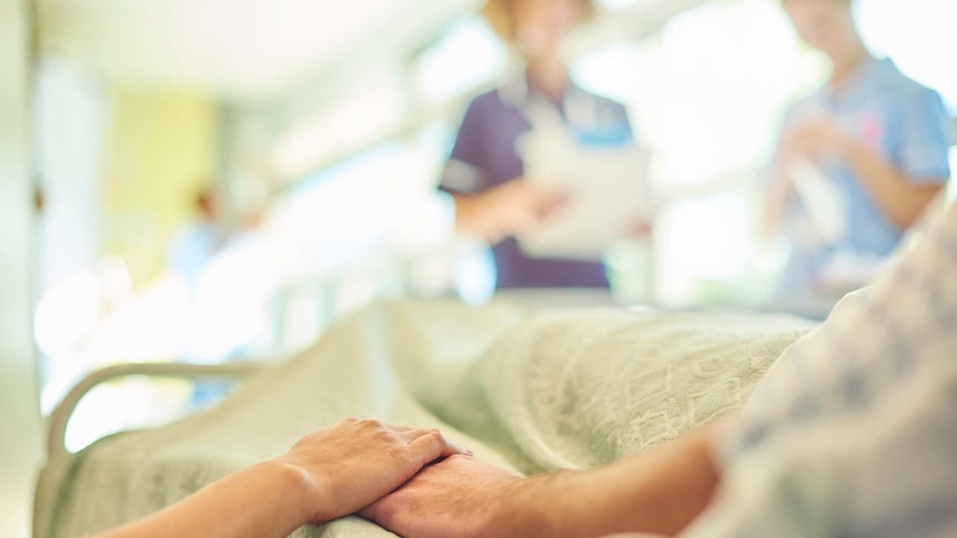 A hand holding the hand of a patient lying in a hospital bed.