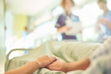 A hand holding the hand of a patient lying in a hospital bed.