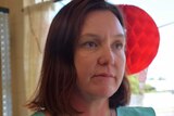 A woman looks out left to right and has Christmas decorations behind her