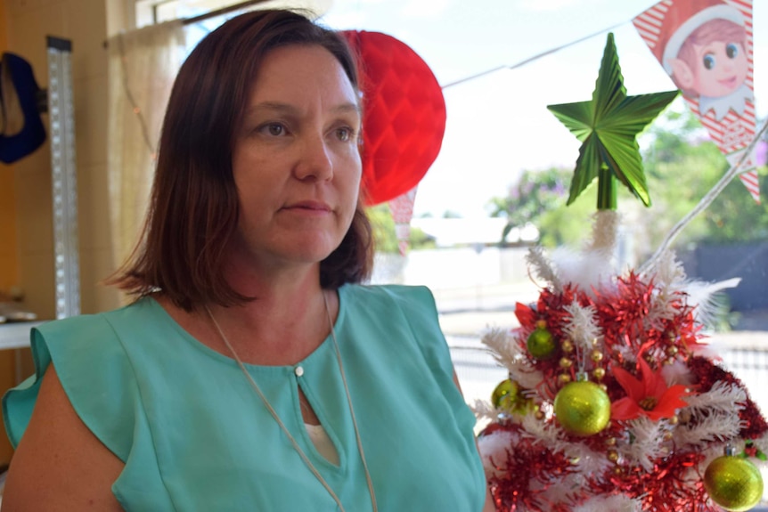 A woman looks out left to right and has Christmas decorations behind her