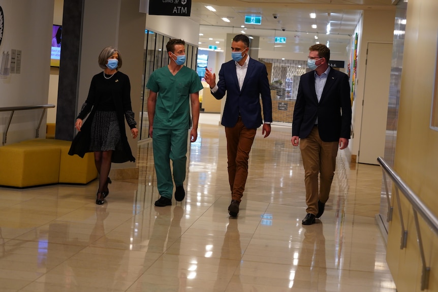 A woman and three men walk down a hospital corridor, all are wearing face masks