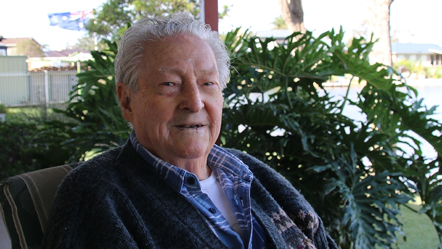 An elderly man sits in a chair outside his retirement home.