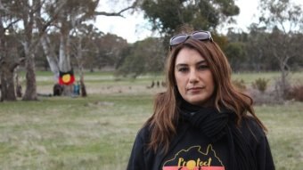 Lidia Thorpe, in an aboriginal flag shirt with the words 'protect country', stands in front of trees.