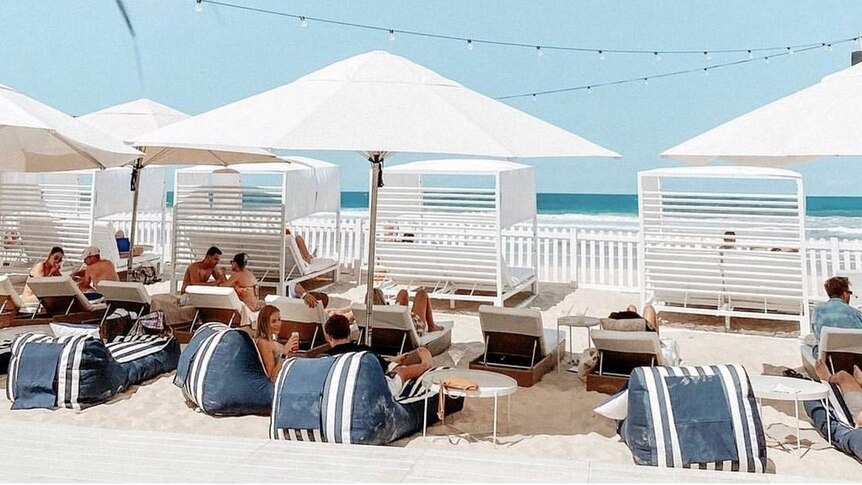 People sitting on lounge chairs under umbrellas at a beach bar.