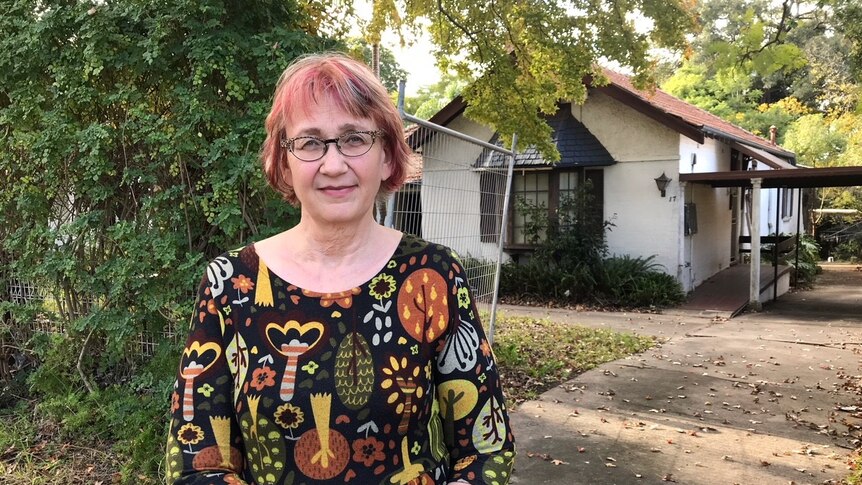A woman with glasses and a colourful dress standing in her driveway.