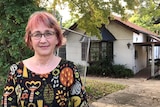 A woman with glasses and a colourful dress standing in her driveway.