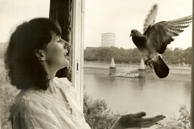 A young Amanda Feilding puts her hands out to catch a pigeon through the window.