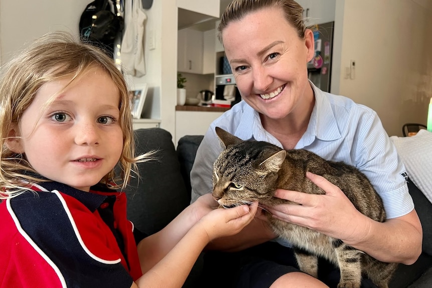 A boy in a school uniform cuddling a cat with his mum.