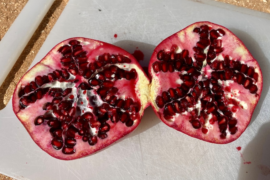 A red pomegranate, cut in half on a white chopping board.