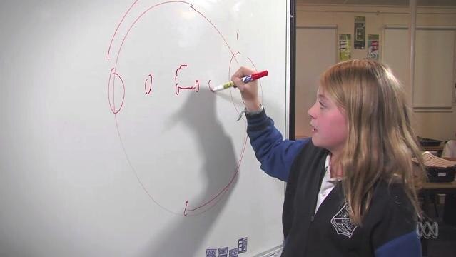 A female primary student draws a diagram on a whiteboard