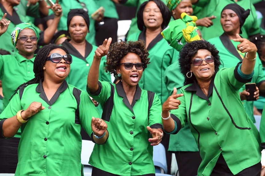 Women in bright green shirts smile and raise their hands at an ANC rally.