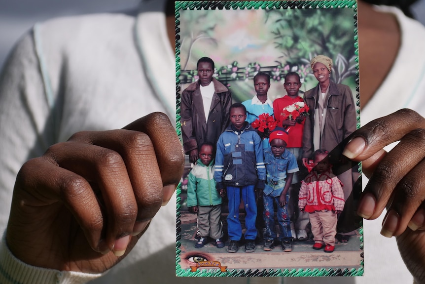 A teenage girl holds up a film photo of a family of eight all looking to the camera, including six children.