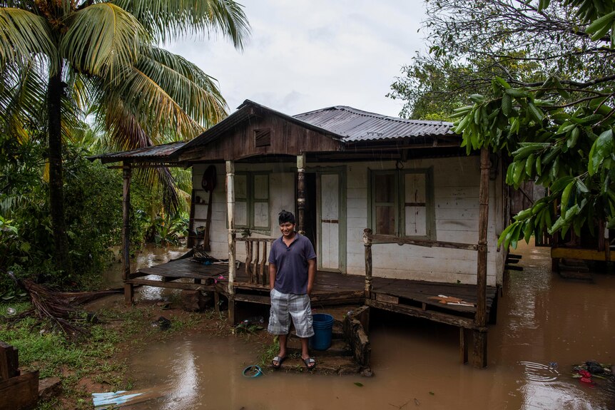 A man stands outside his house which is surrounded by floodwaters. 