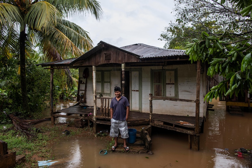 A man stands outside his house which is surrounded by floodwaters. 