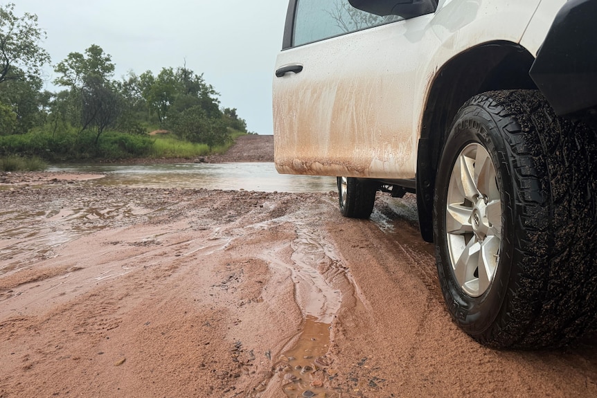 A muddy car on a dirt road with a water crossing