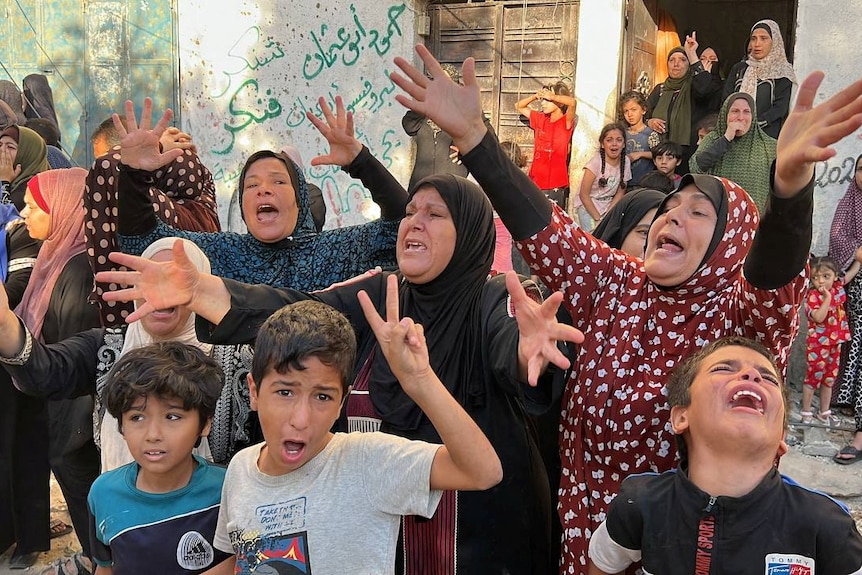 Women and children hold out their arms crying and yelling at the site of an air strike. 