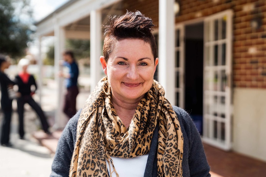 A head and shoulders shot of a smiling woman with short dark hair and a leopard print scarf standing outside posing for a photo.