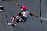 Arisa Trew on a skating ramp wearing a pink helmet with her arms spread out standing on an angle on a skateboard.