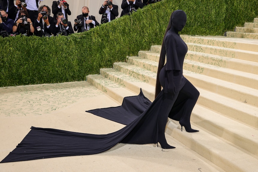Kim Kardashian wears all black outfit including full covering face mask and cape.