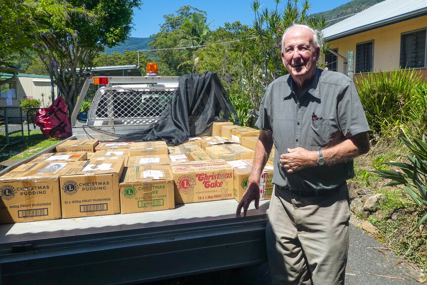 A man stands next to the tray of a ute which has a bunch of boxes on it. He is smiling.
