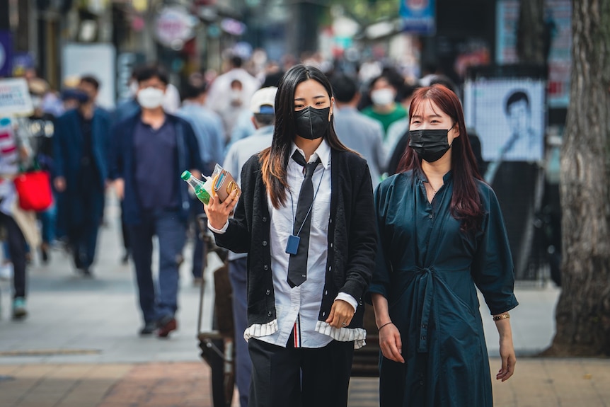 Two Korean young people in masks walking on a busy street 