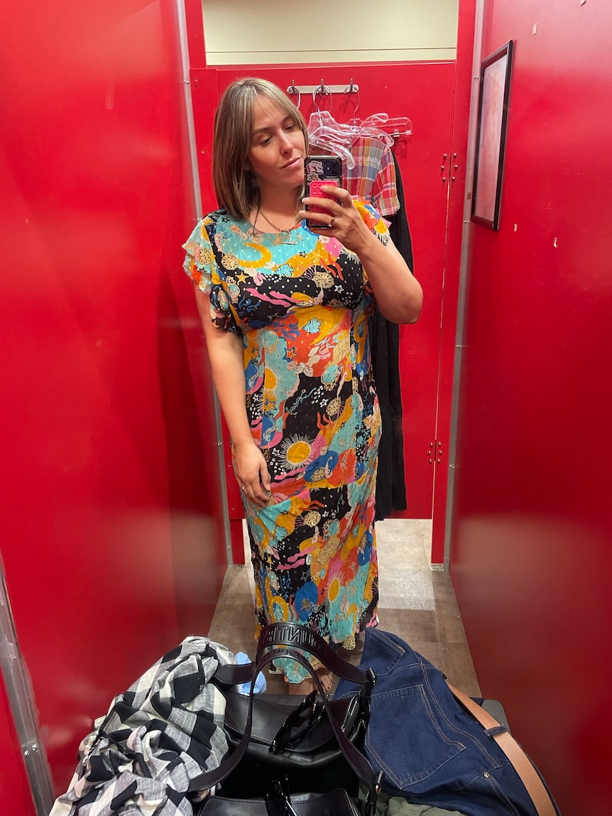 Op-shopper Bec Brewin takes a phone photo in an op shop change room while wearing a bright maxi dress.